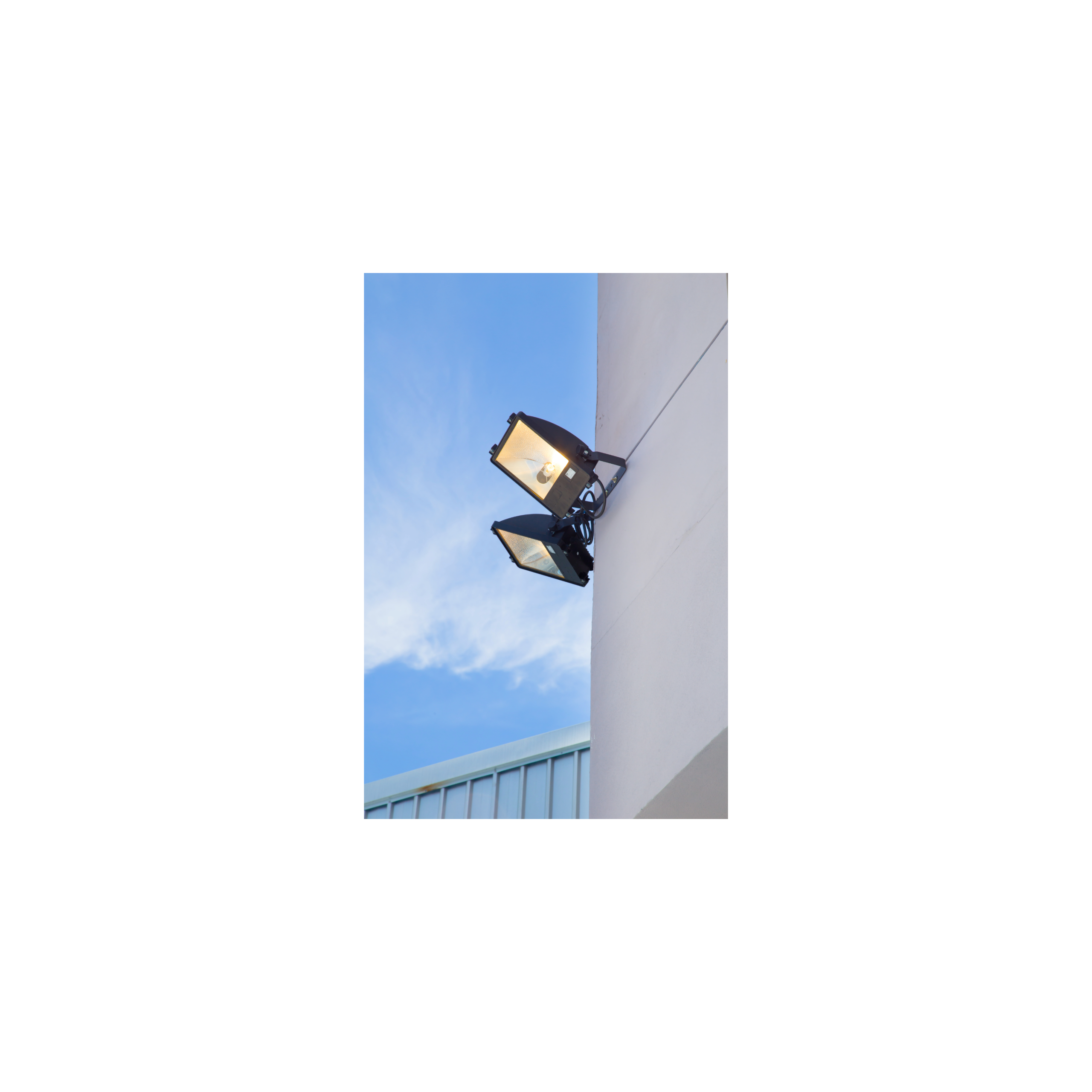 Two exterior floodlight fixtures mounted on a commercial building